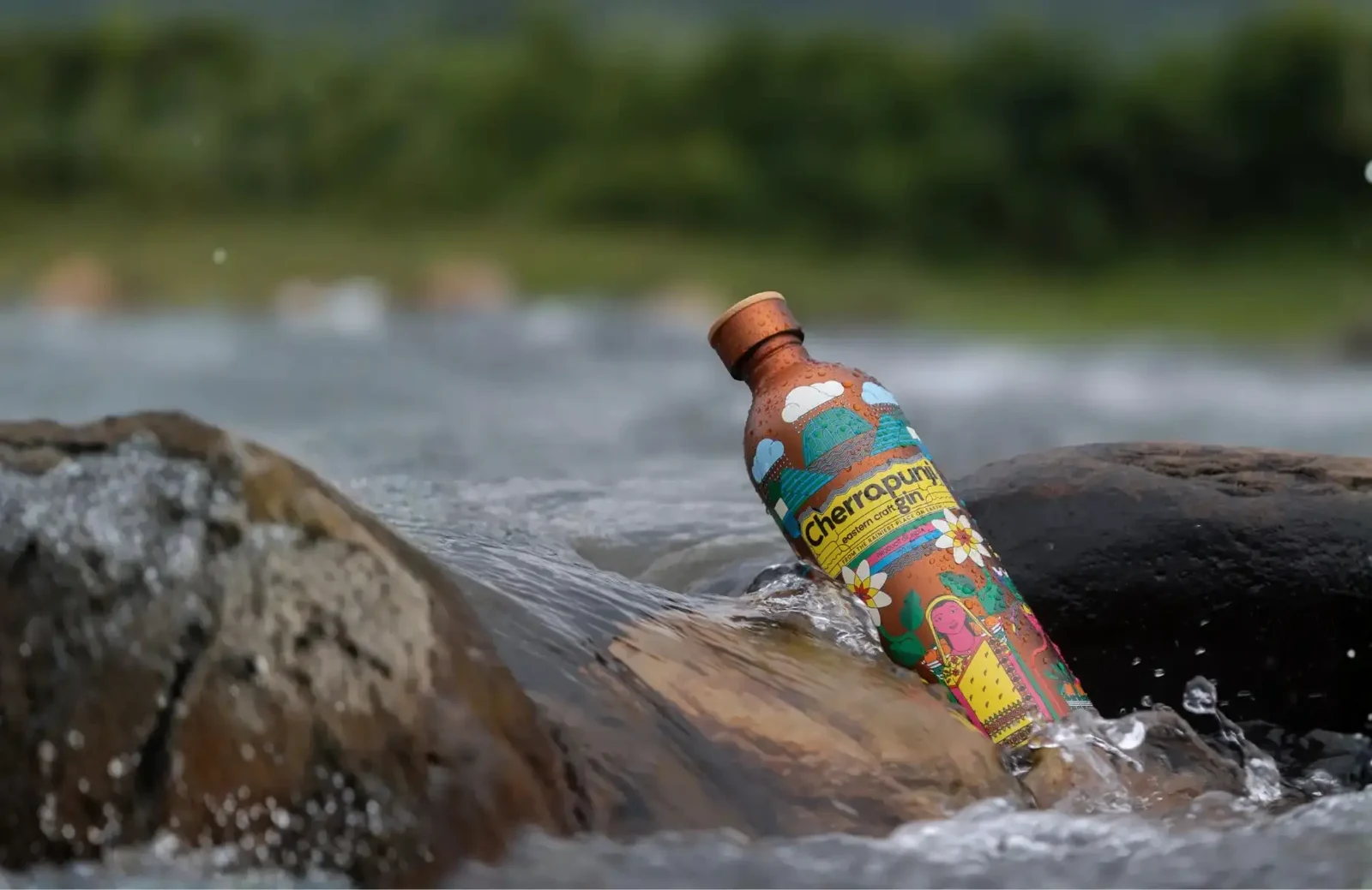 Cherrapunji Gin’s illustrated bottle photographed among rocks and flowing water.